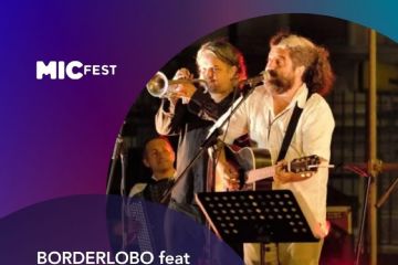 Al centro della locandina, si trova una foto scattata durante un concerto dal vivo. Mostra i musicisti sul palco sotto le luci: in primo piano c'è un uomo con la barba che canta e suona la chitarra acustica, dietro di lui un trombettista e, parzialmente visibile sullo sfondo, un altro musicista.
In alto a sinistra compare il logo "MICFEST", scritto in bianco con un carattere moderno.
Nella parte centrale sono riportati i dettagli dell'evento: "BORDERLOBO feat RAFFAELE KOHLER" (i protagonisti della serata); "Canzoni di frontiera da Dylan a De André" (il tema o titolo del concerto); "La cult band tex mex di Alex Gariazzo e Andrea Parodi" (una breve descrizione del gruppo).
Quindi, nella parte inferiore, sempre con testo bianco ben leggibile, sono indicati la data, il luogo e le modalità di accesso: Domenica 19 luglio - 21:30 a Castelnuovo Magra (SP), Piazza Querciola, con Ingresso gratuito fino a esaurimento posti.
