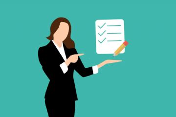 una donna con vestito nero e camicia bianca, capelli lunghi marroni espone una scheda bianca con una matita