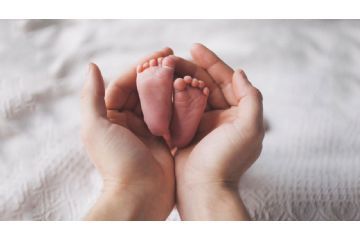 sfondo bianco, due mani di adulto che tengono due piedini di neonato