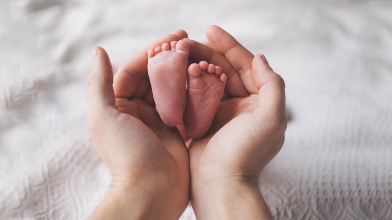 sfondo bianco, due mani di adulto che tengono due piedini di neonato